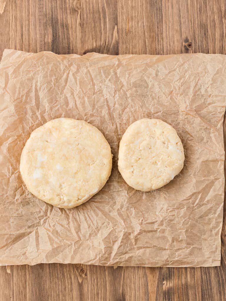 Two rounds of pie dough on beige parchment paper. Wooden background.