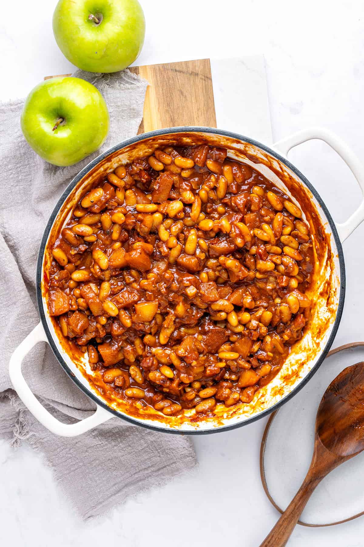 Top view white pot with baked beans, apples and bacon. White and gray background. Green apples.