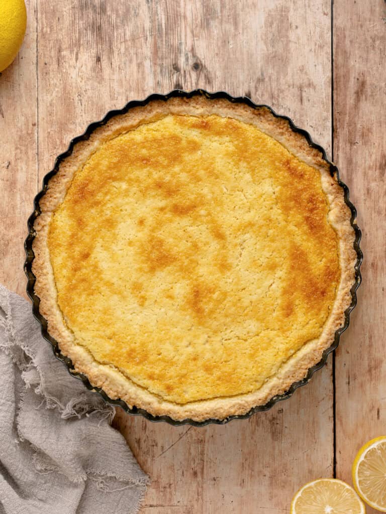 Baked ricotta pie in a dark round pie pan. Wooden surface.