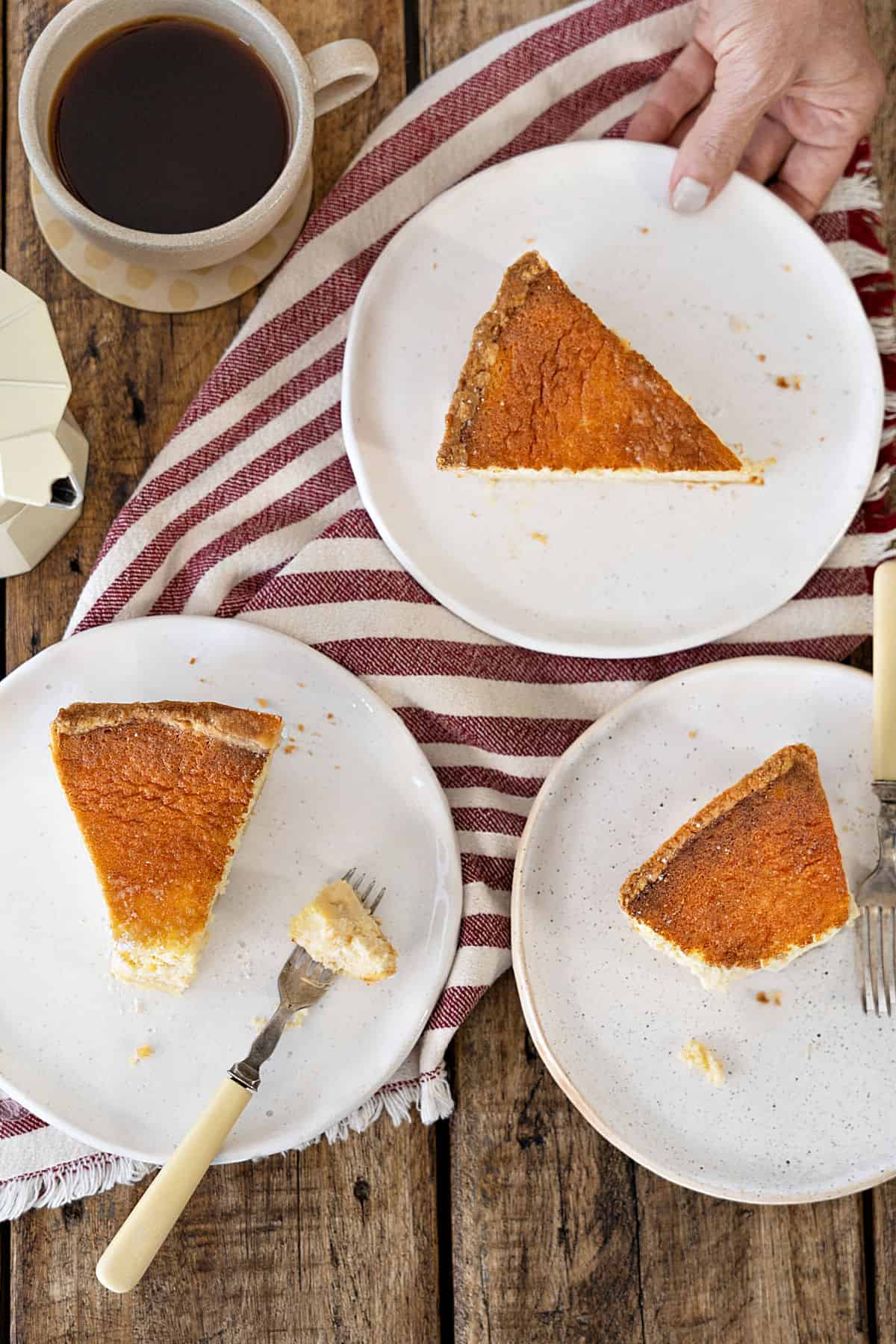 Three white plates with ricotta pie slices. Red striped cloth. Wooden surface. Top view.