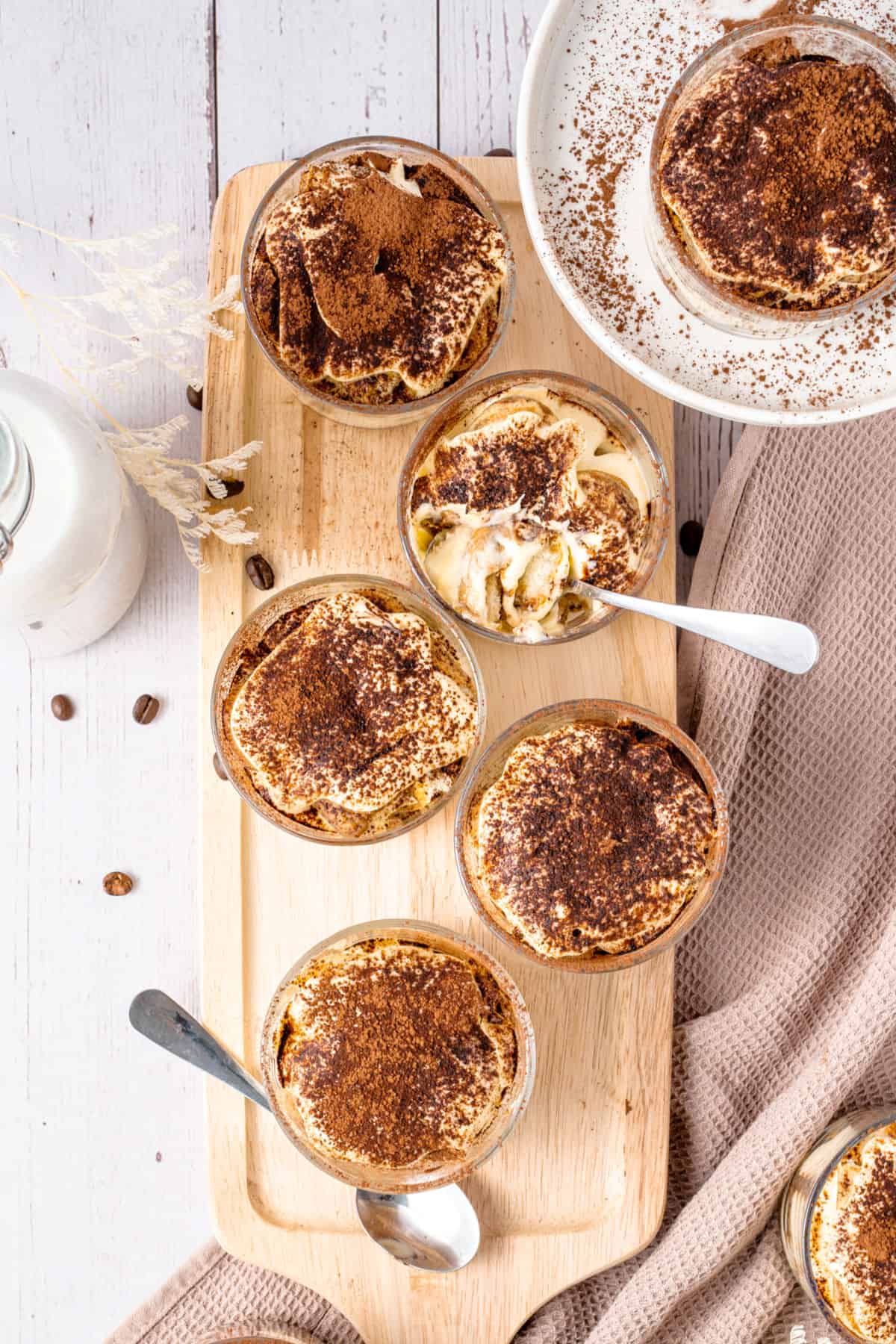 Wooden board with several cocoa dusted tiramisu cups. White beige surface.