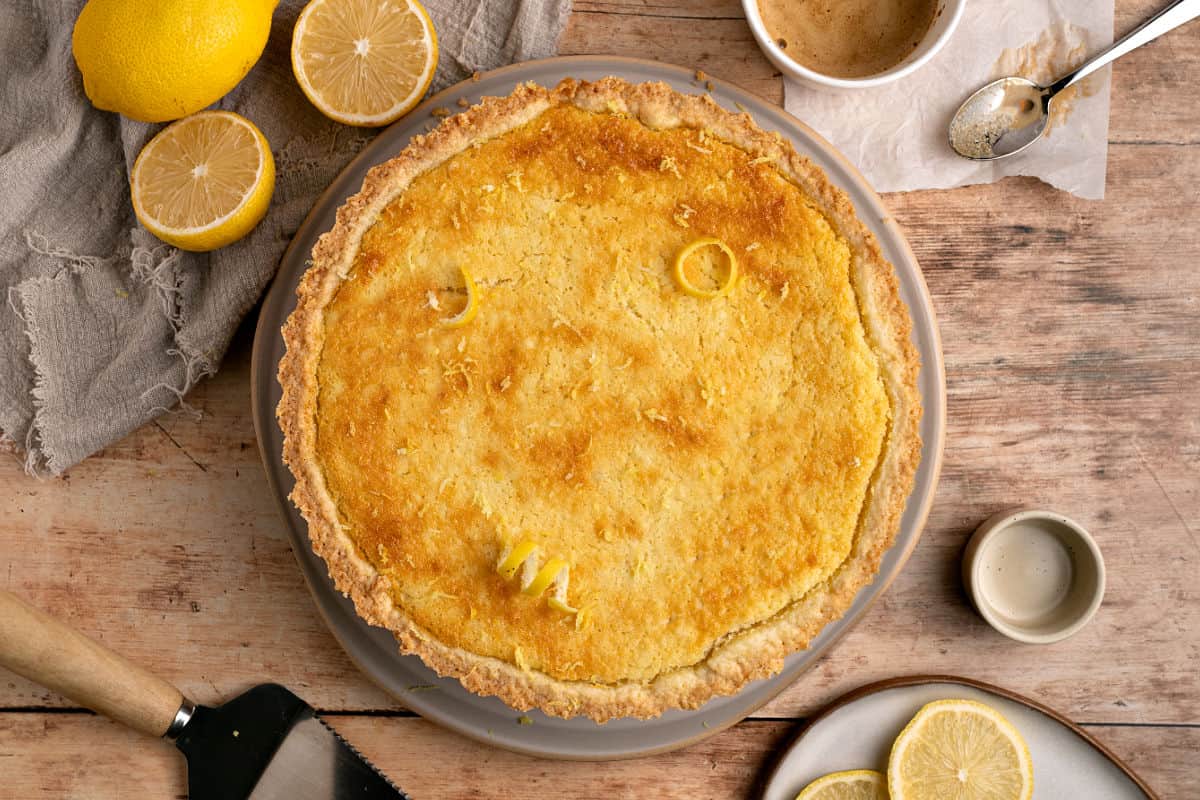 Pie plate with ricotta pie, wooden table, lemons, gray towel.