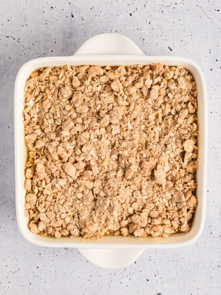 Square white dish with applesauce crisp before baking. Light gray background.