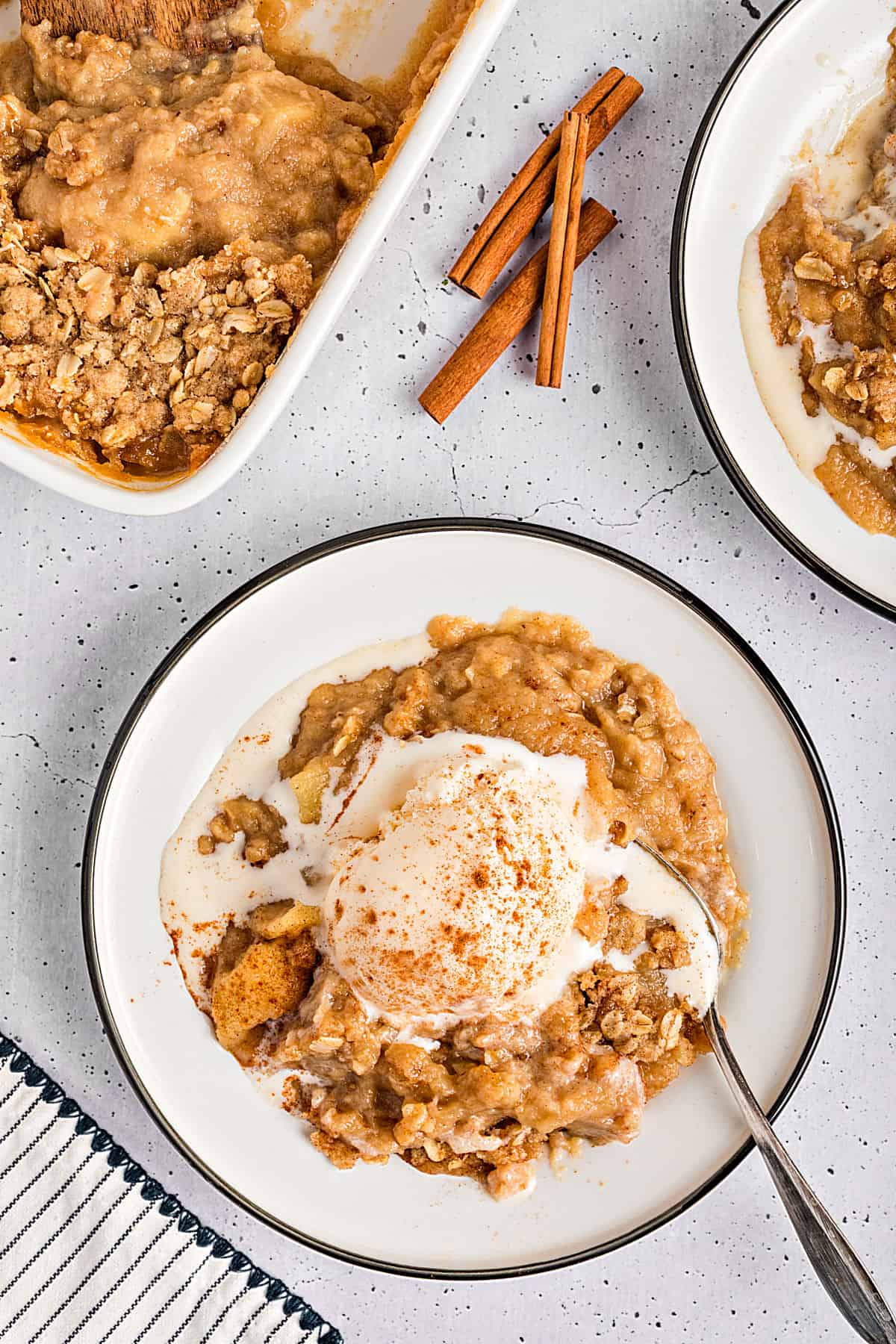 Light gray background with black-rimmed white plates of applesauce crisp servings with ice cream.