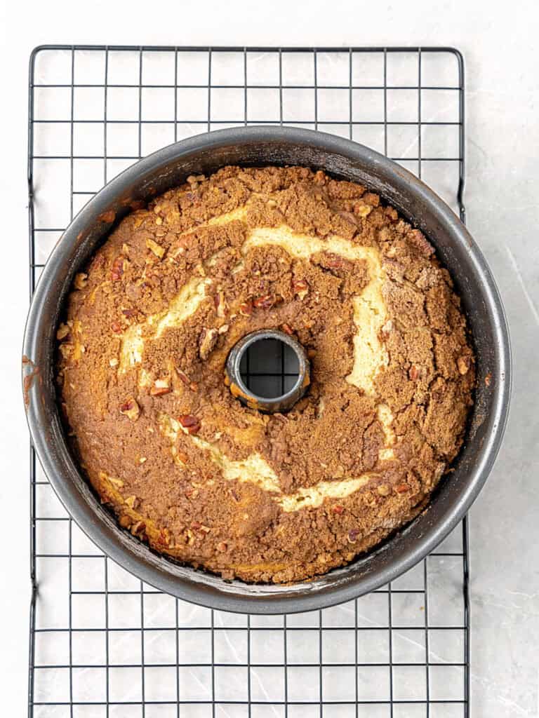 Baked cinnamon coffee cake in a tube pan on a wire rack. Light grey surface.