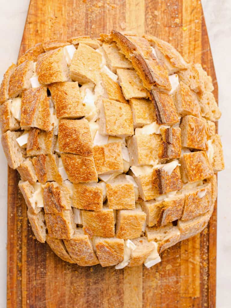 Wooden board with brie stuffed bread loaf with crisscross cuts.