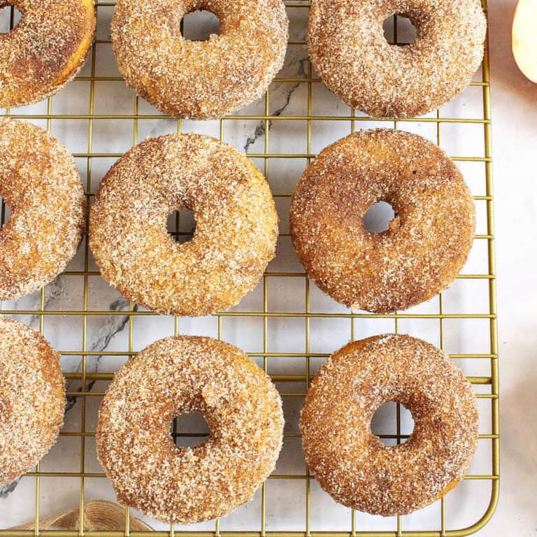 Three rows of apple cider donuts with cinnamon sugar coating on a wire rack.
