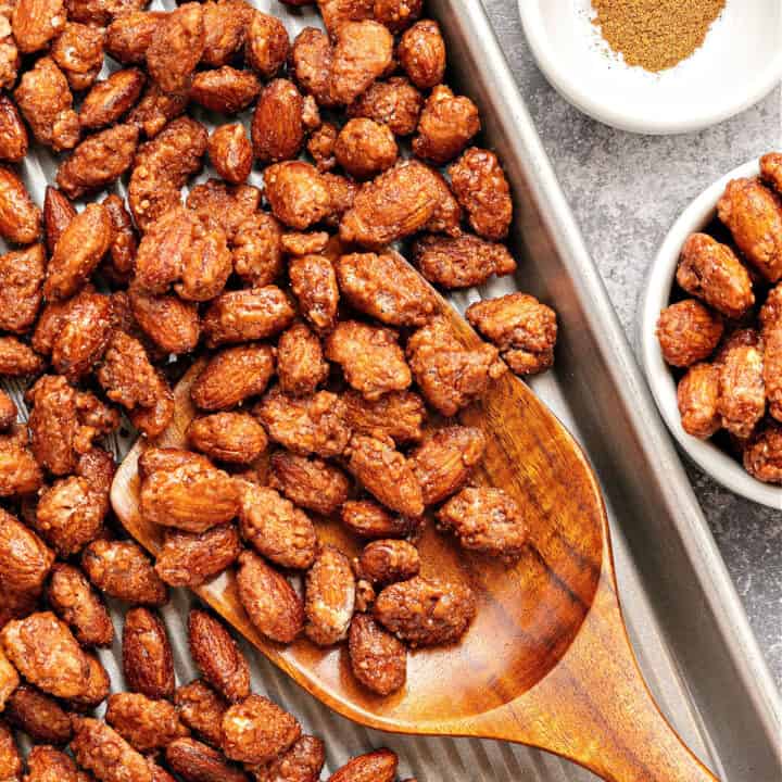 Wooden spoon of candied almonds on a metal sheet. Bowl with spices.