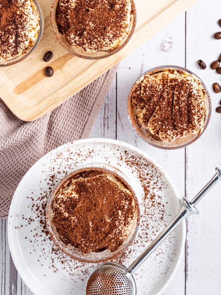 Top view of tiramisu glasses on a white plate and board. White vintage background.