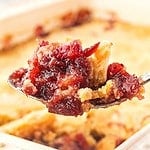 Red and white text overlay on a spoon of cranberry dump cake.