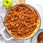 White pot with baked beans, apples and bacon. White and gray background. Green apple.