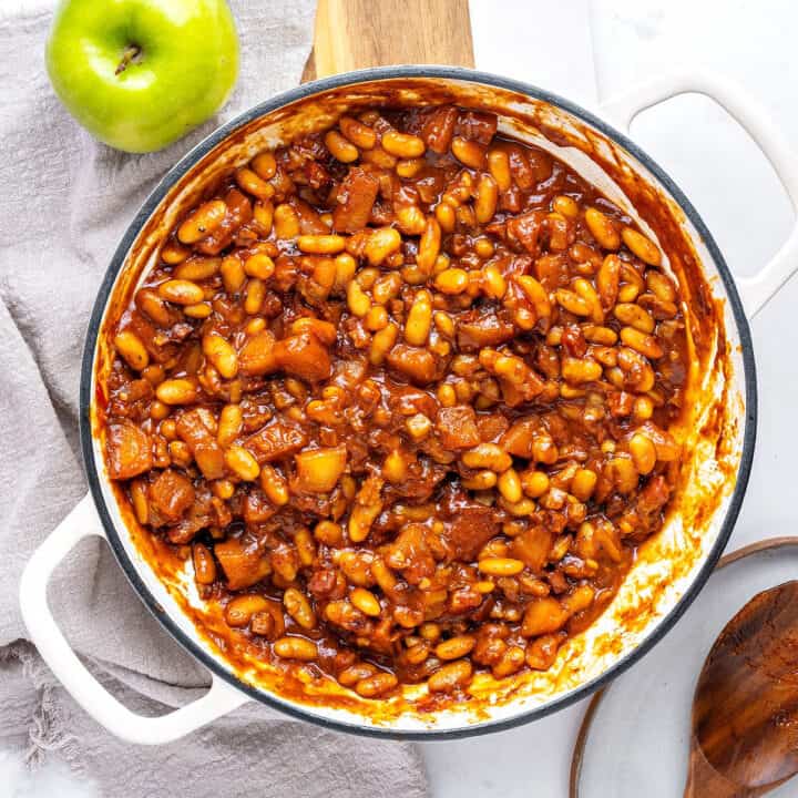 White pot with baked beans, apples and bacon. White and gray background. Green apple.