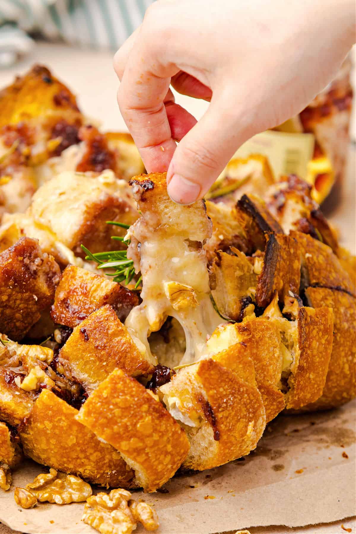 Pulling piece of bread with melted cheese from round loaf.