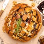 Round loaf with brie and jam between crisscross slits. Rosemary sprig. Parchment paper.