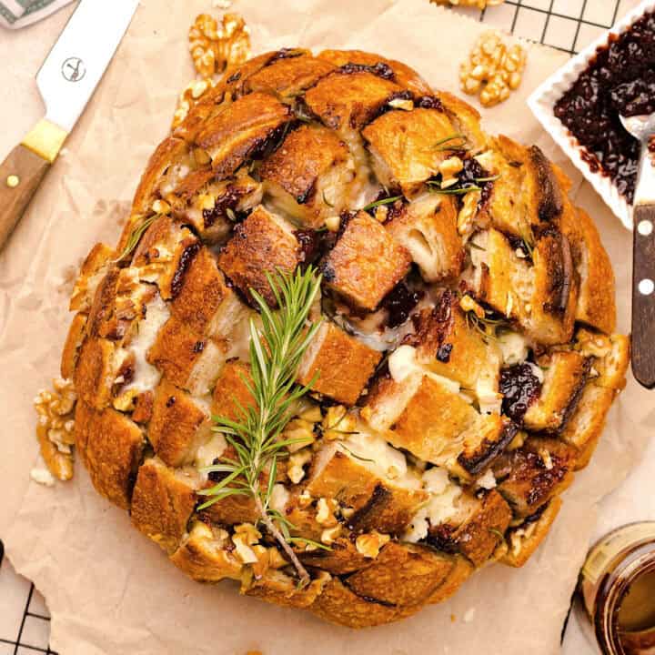 Round loaf with brie and jam between crisscross slits. Rosemary sprig. Parchment paper.