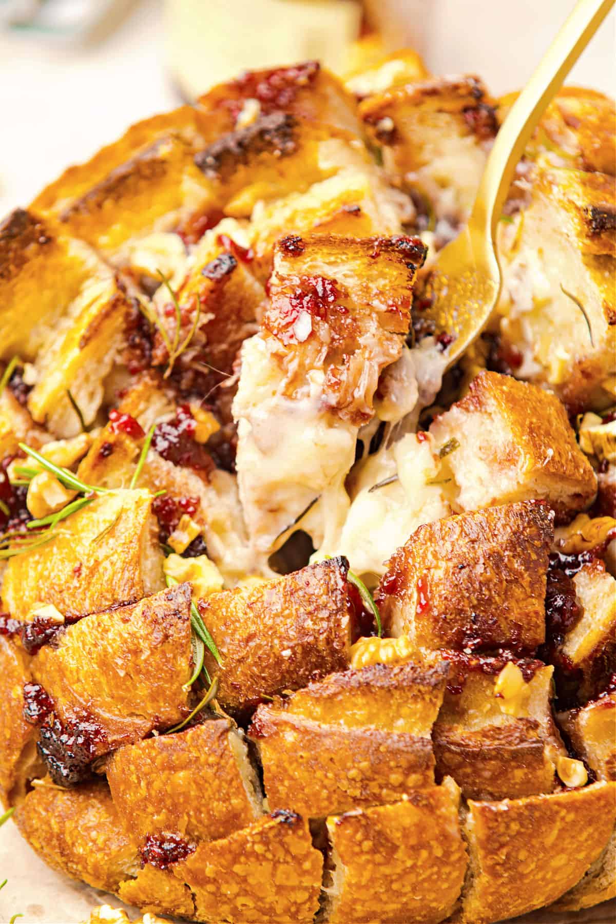 Pulling piece of cheesy bread with a fork from a whole loaf.