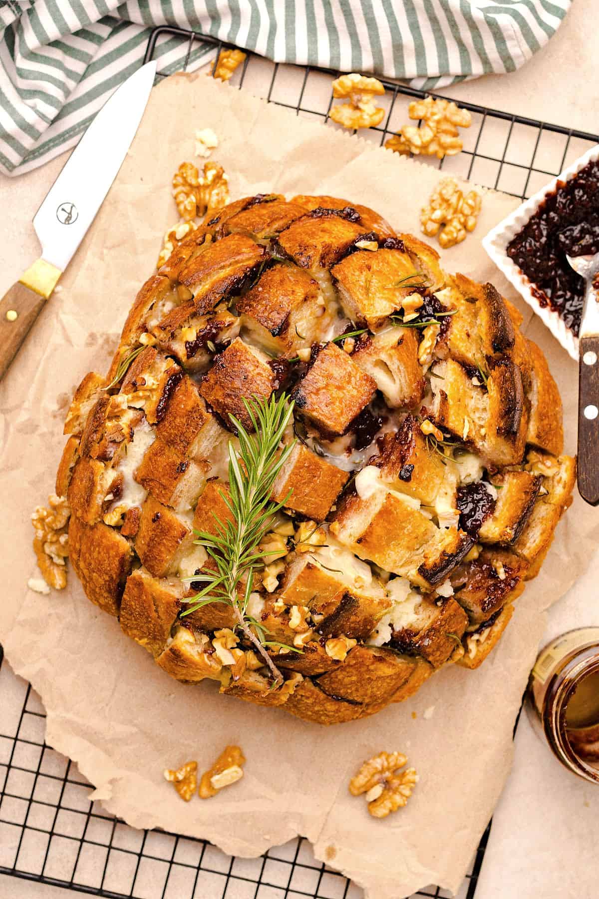 Top view of round loaf with brie and jam between slits. Rosemary sprig. Parchment paper and rack surface.