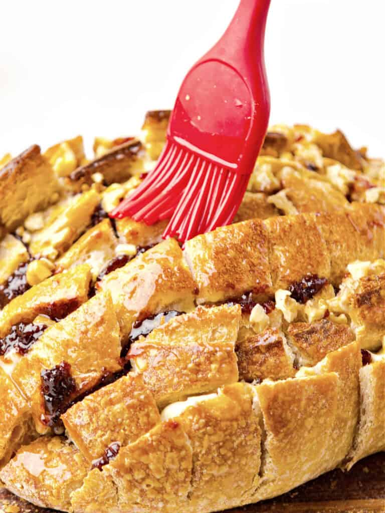 Brushing melted butter with red silicon brush on pull apart bread loaf.
