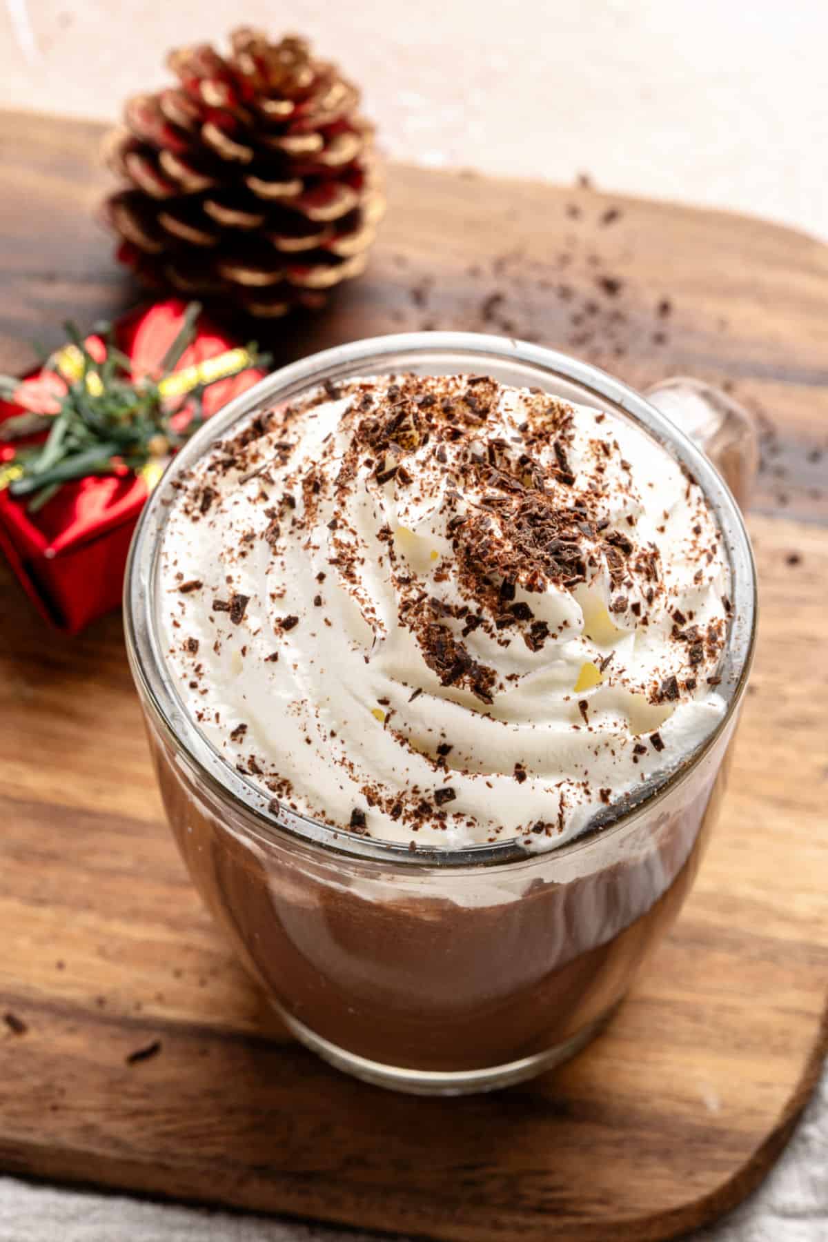 Wooden board with cream-topped hot chocolate mug. Pine cone.