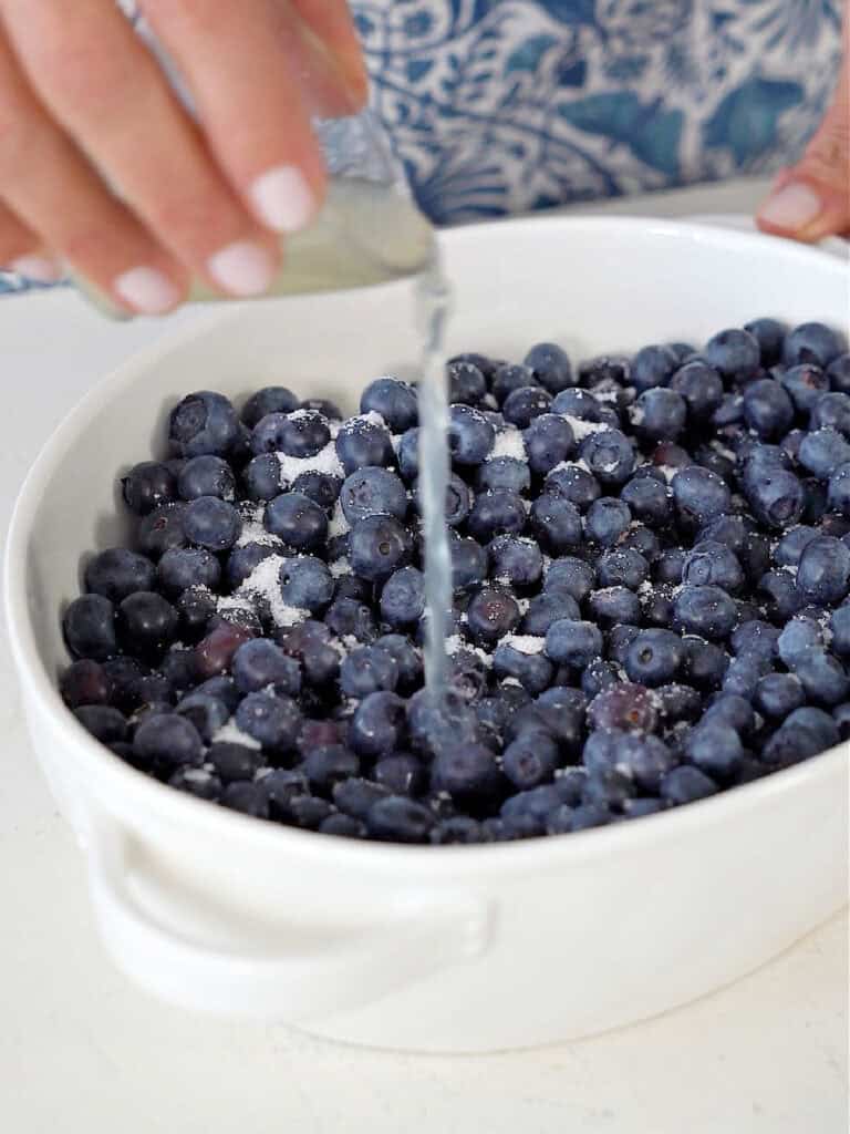 Drizzling lemon juice over blueberries in a white oval dish.