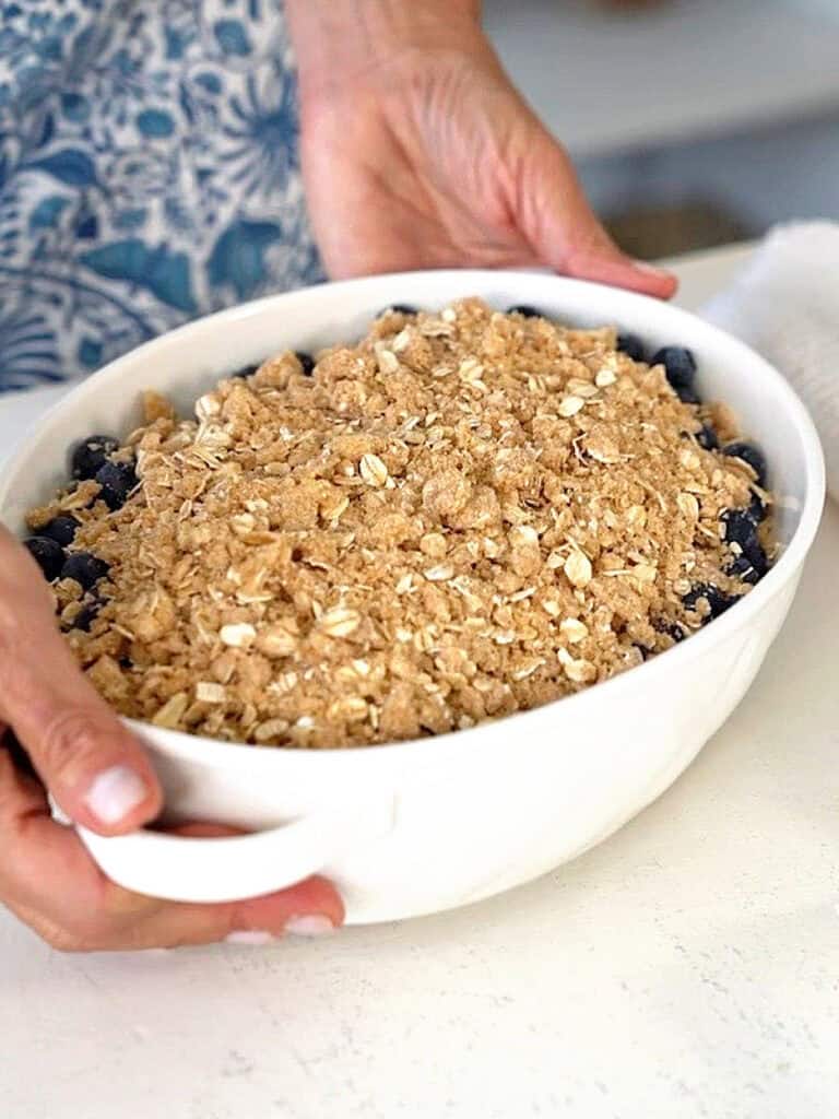 Oval white baking dish with blueberry oat crisp before baking.
