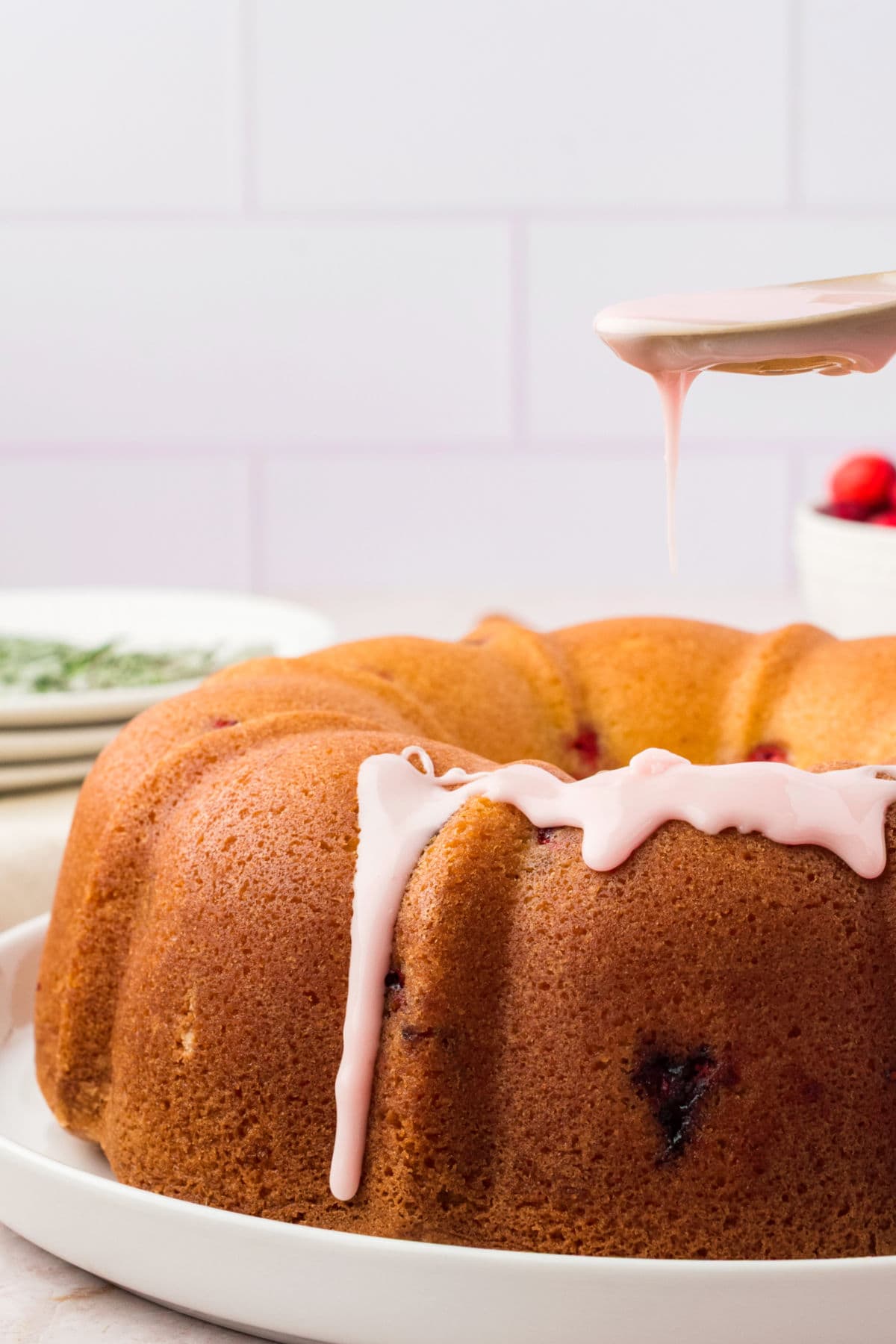 Glazing bundt cake with cranberry glaze. White tile background.