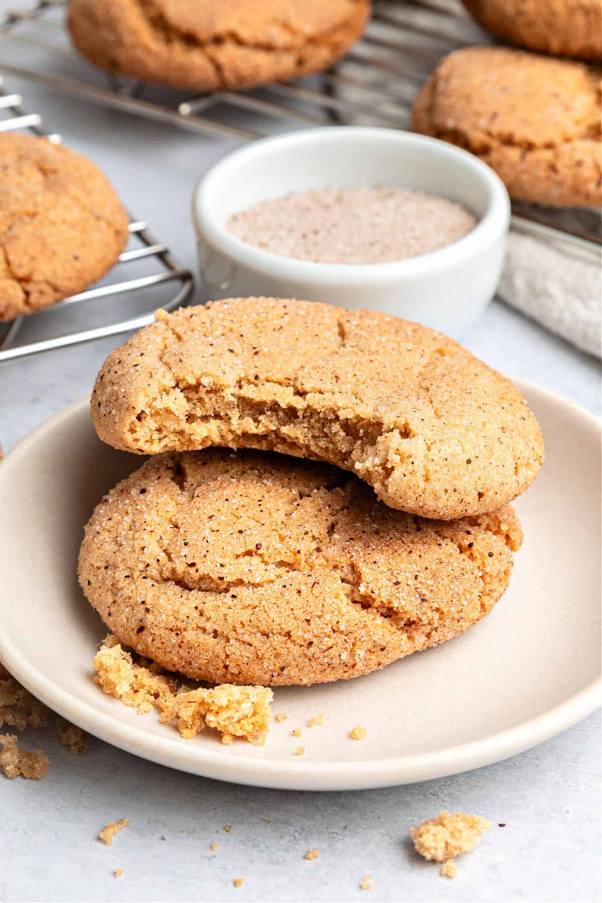 Light pink plate with whole and bitten cinnamon snickerdoodle cookies. Bowl with sugar.