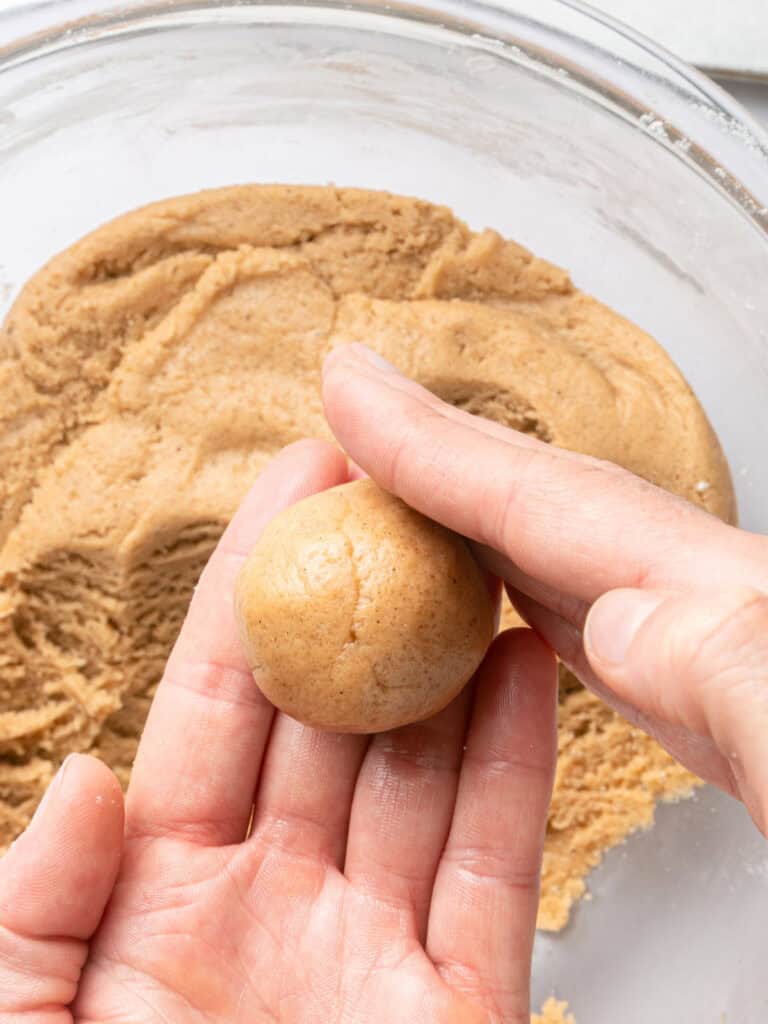 Forming cookie dough ball with palms. Bowl with dough below.