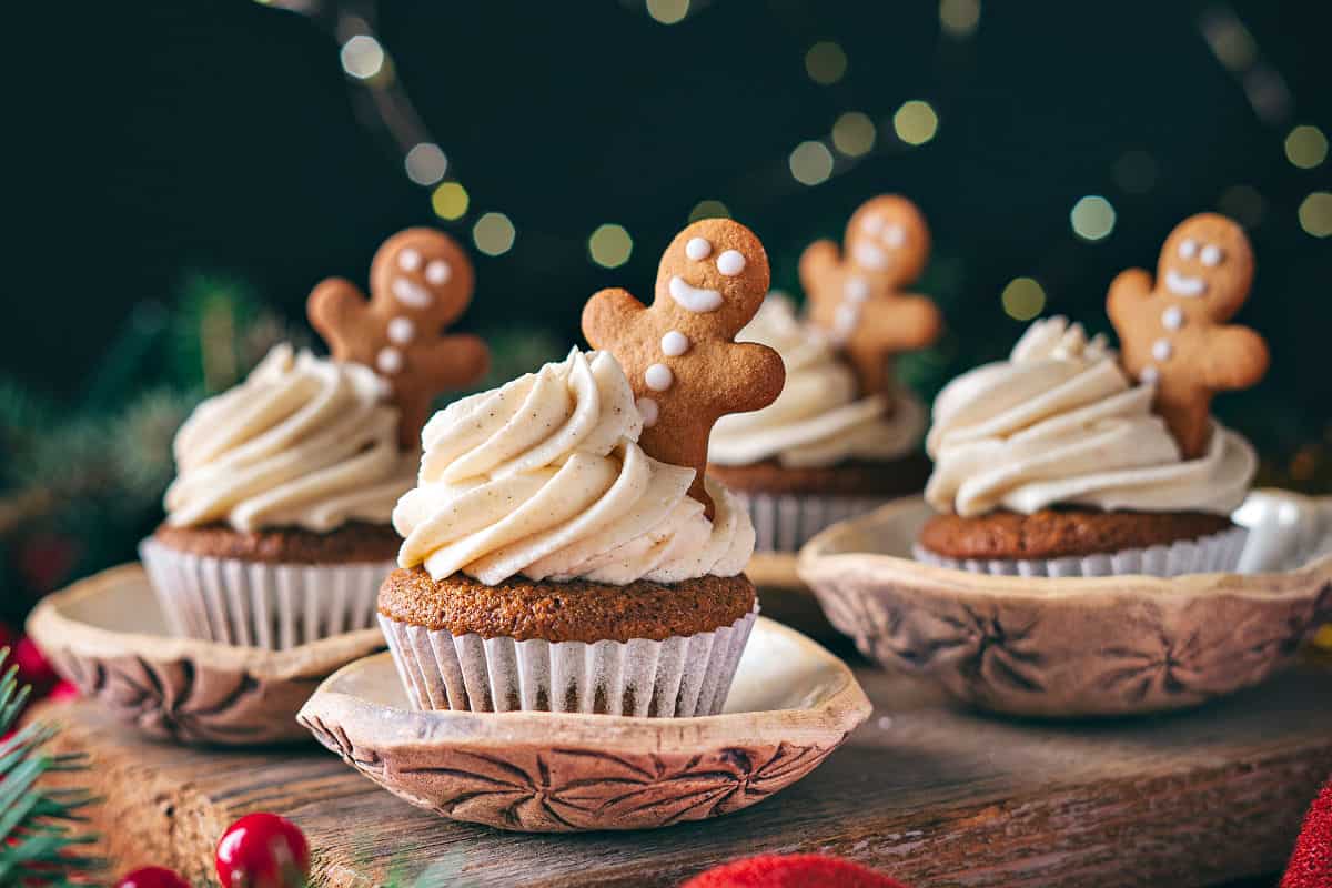 Several frosted gingerbread cupcakes in paper liners. Cookie decorations.