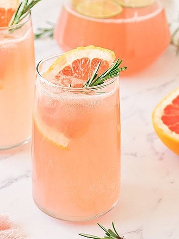 White marble with tall glasses of grapefruit cocktail. Fruit slices, rosemary sprigs.