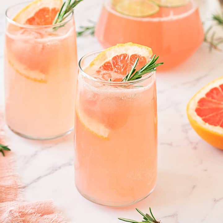 White marble with tall glasses of grapefruit cocktail. Fruit slices, rosemary sprigs.