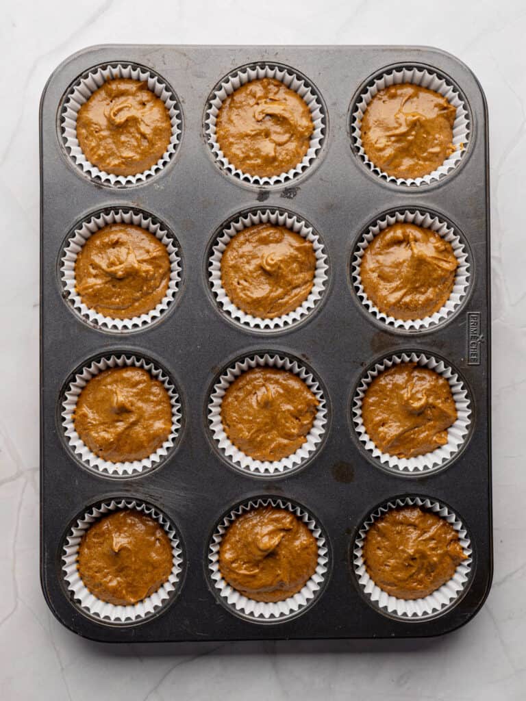 White paper liners in a metal pan with gingerbread cupcake batter.