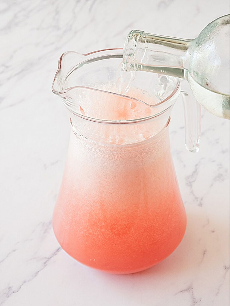 Pouring gin into a glass pitcher with grapefruit juice.