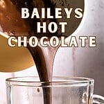 Pink, brown and white text overlay on hot chocolate poured into a glass mug.