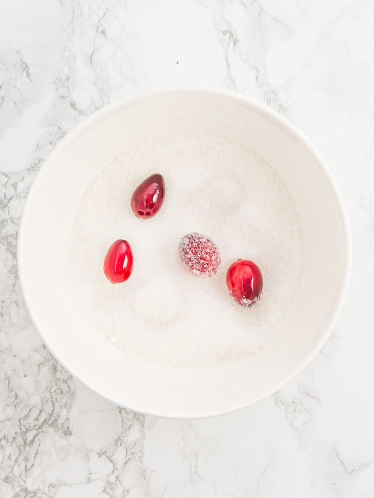 Rolling cranberries in sugar in a white bowl.