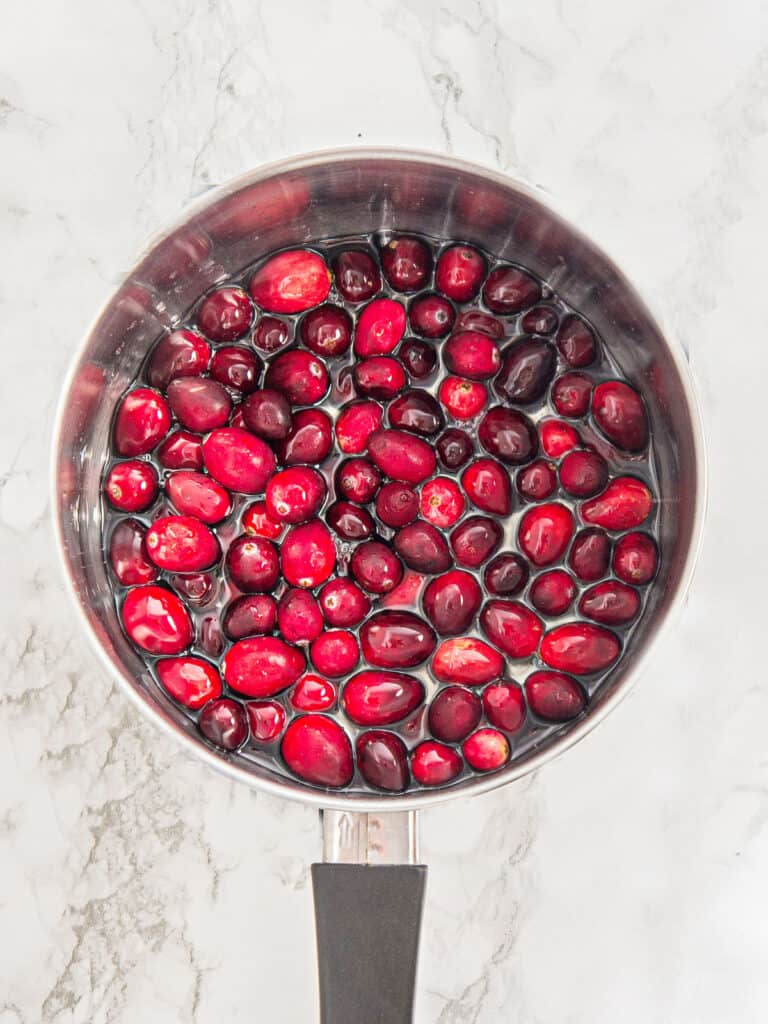 Cranberries in syrup in a metal saucepan. White marble surface. 