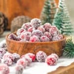 Bunch of sugared cranberries in a wooden bowl and white paper. Christmas decor in the background.