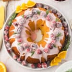 Sugared cranberries on glazed bundt cake. White plate and background. Orange slices.
