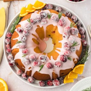 Sugared cranberries on glazed bundt cake. White plate and background. Orange slices.