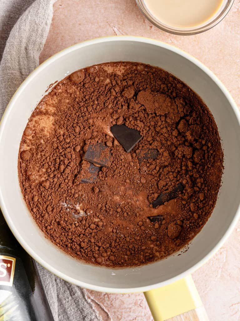 White saucepan with ingredients for hot chocolate. Pinkish gray background.