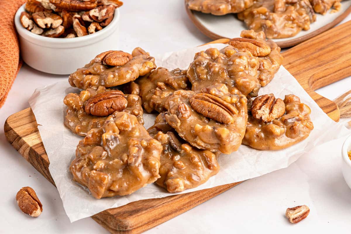 Wooden and white surface with pile of pecan pralines. Bowl of pecans.