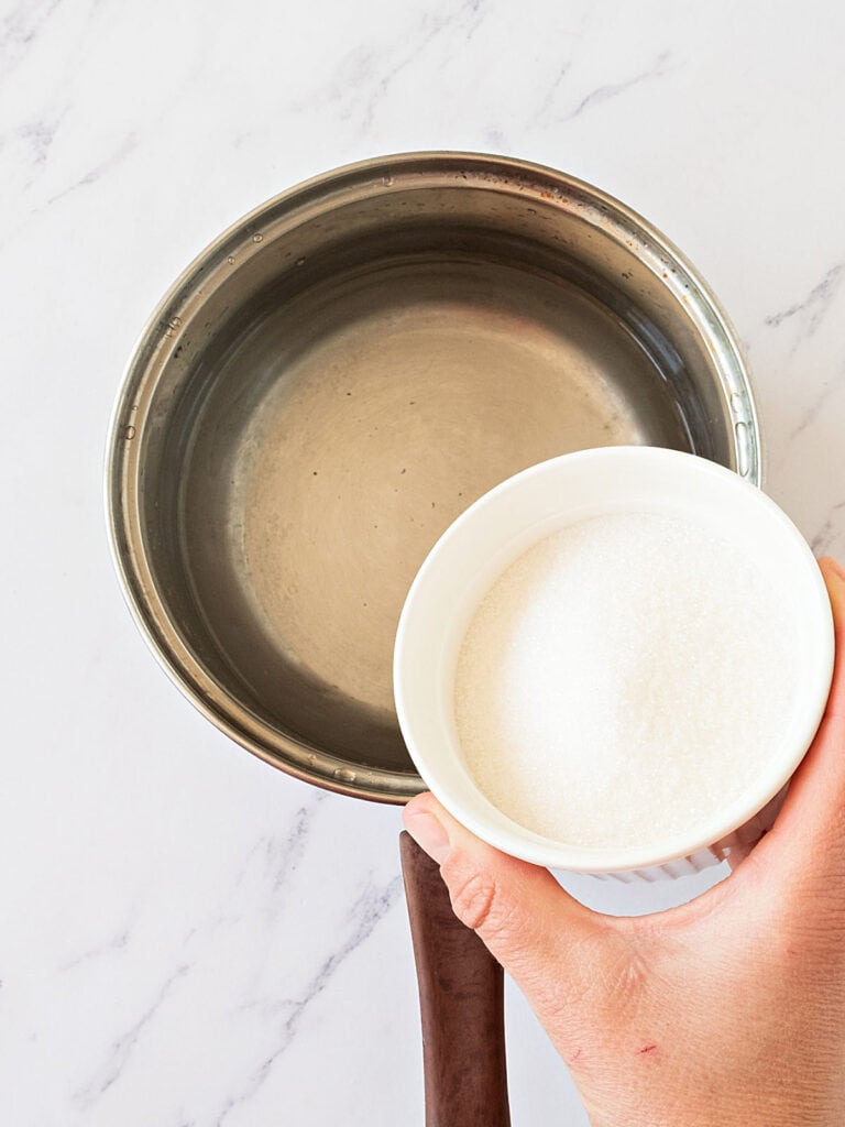 Adding sugar to metal saucepan with water. Marbled background.