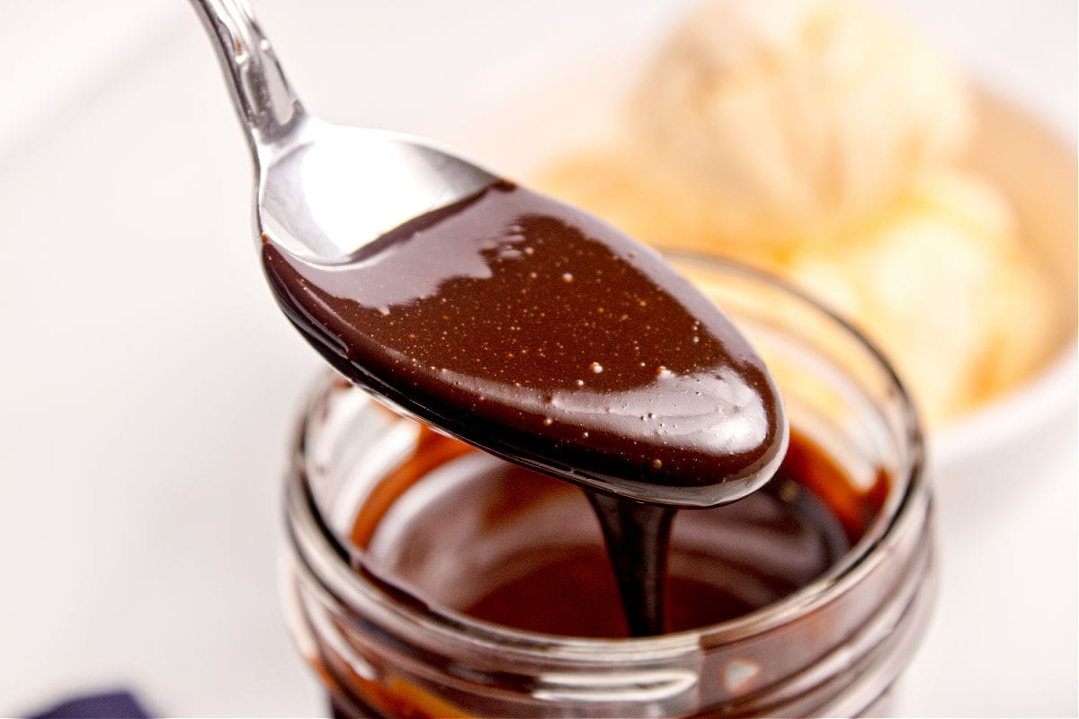 Jar with chocolate sauce being spooned. White yellow background.