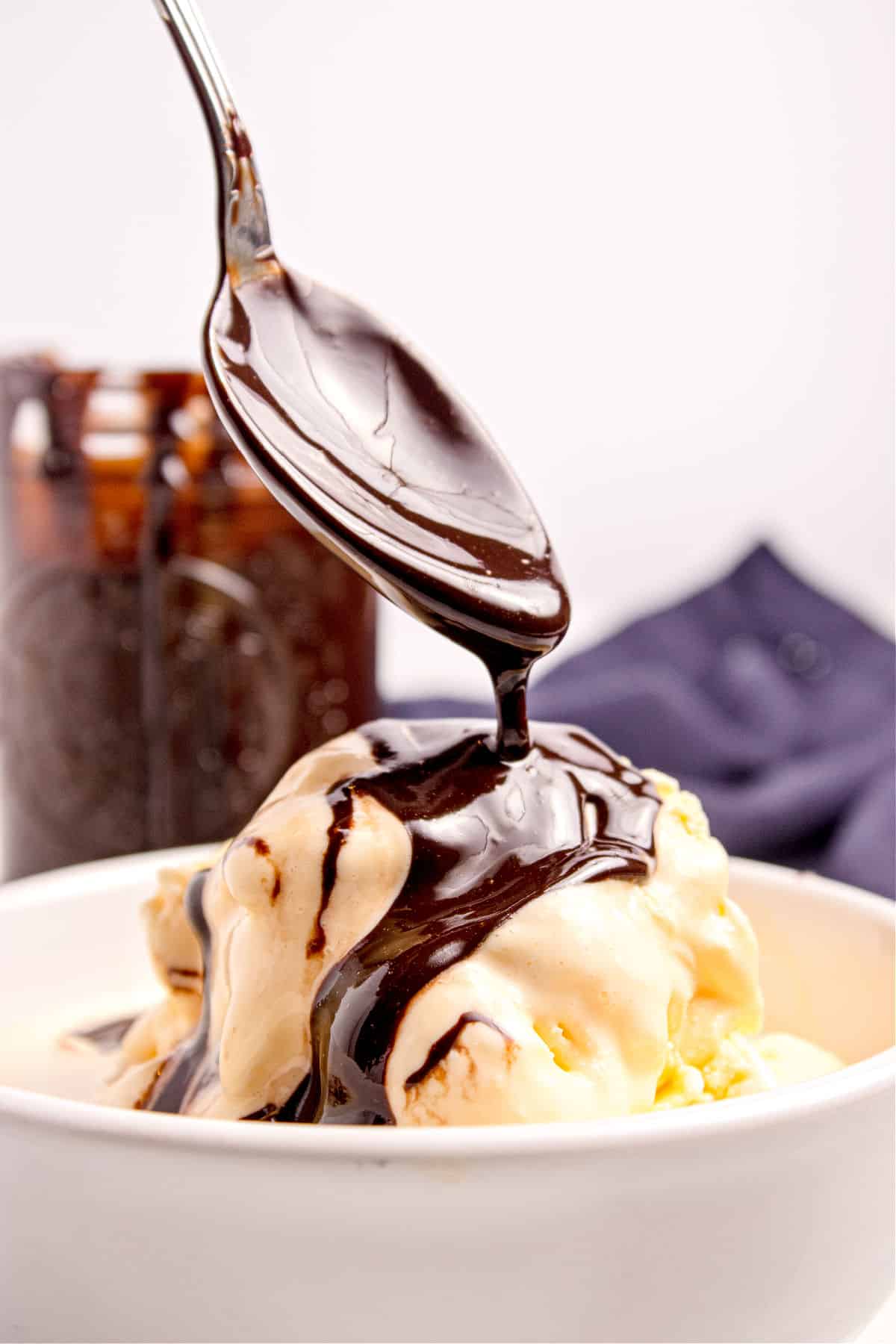 Spooning chocolate sauce onto vanilla ice cream in a white bowl.