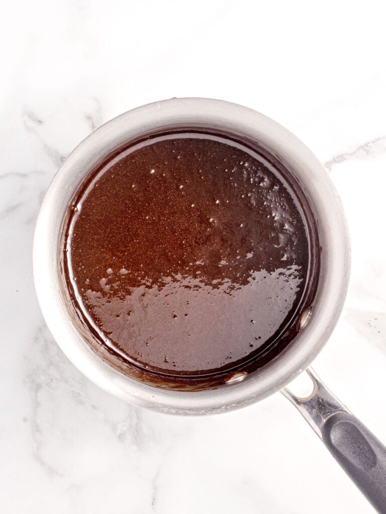 Marble surface with chocolate sauce in a metal saucepan.