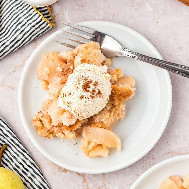 Serving of pear cobbler with ice cream on a white plate. Silver fork.
