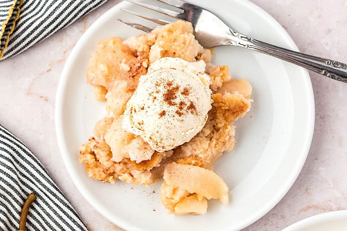 White plate of pear cake mix cobbler serving with ice cream. Silver fork.