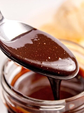 Close up silver spoon with chocolate sauce over glass jar.