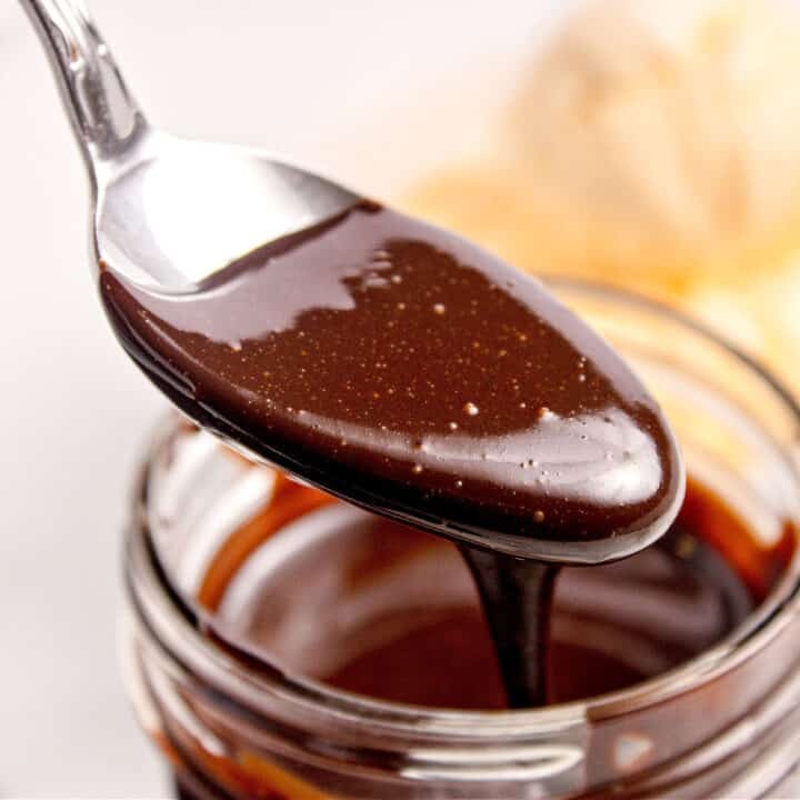 Close up silver spoon with chocolate sauce over glass jar.