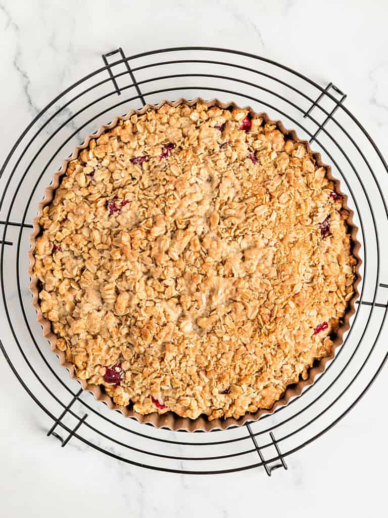 Baked crumble apple cran pie on a wire rack. White marble background.